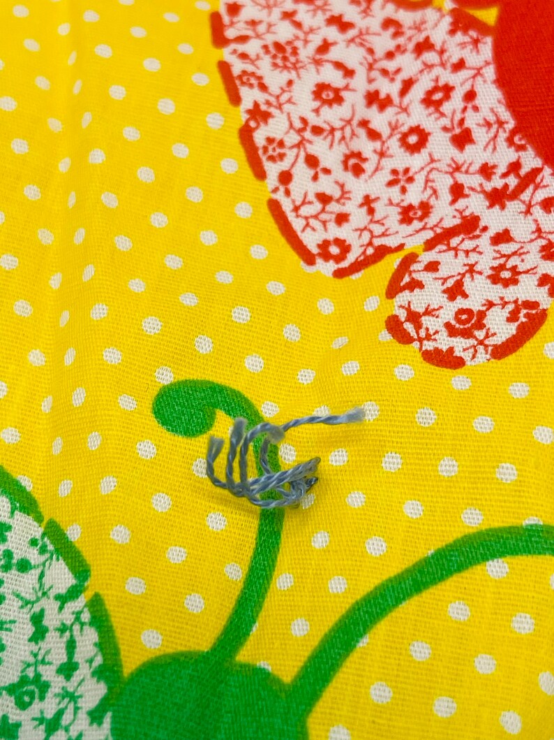 May include: A close-up of a blue and gray string on a yellow fabric with white polka dots and a red and white floral pattern.