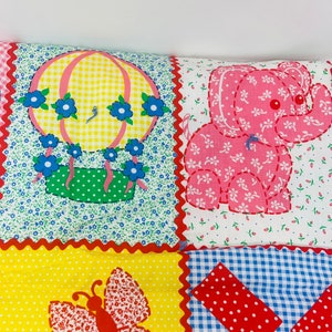 May include: A patchwork quilt with a hot air balloon, elephant, butterfly, and windmill design. The quilt is made of different fabrics with various patterns, including gingham, polka dots, and floral prints. The colors are bright and cheerful, including red, yellow, blue, green, and pink.