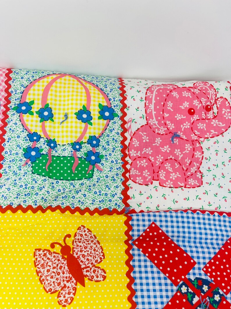 May include: A patchwork quilt with a hot air balloon, elephant, butterfly, and windmill design. The quilt is made of different fabrics with various patterns, including gingham, polka dots, and floral prints. The colors are bright and cheerful, including red, yellow, blue, green, and pink.