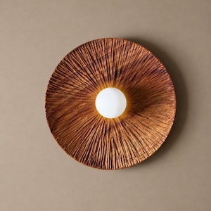May include: A round, wooden wall sconce with a textured, radial design. The sconce has a warm, brown color and features a central, spherical, white light fixture. The light fixture is a bright, glowing orb.