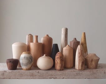 May include: A collection of wooden vases in various shapes and sizes, with natural wood grain patterns and colors ranging from light brown to dark brown. Some vases have a more polished finish, while others have a more rustic look.