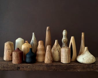 Peut inclure: Une collection de sculptures en bois faites à la main, de formes et de tailles variées. Les sculptures sont exposées sur une étagère en bois brun foncé, sur fond brun foncé. Les tons de bois varient du beige clair au brun foncé.