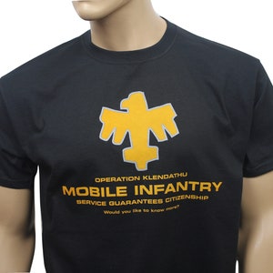 May include: Black t-shirt featuring a yellow eagle logo and the text "Operation Klendathu Mobile Infantry Service Guarantees Citizenship Would you like to know more?"