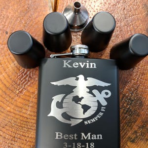 May include: Black engraved flask with a silver eagle, anchor, and globe design. The flask is personalized with the name "Kevin", the text "Best Man", and the date "3-18-18". The flask comes with four shot glasses and a funnel.