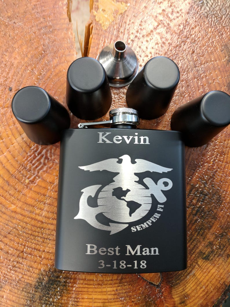 May include: Black engraved flask with a silver eagle, anchor, and globe design. The flask is personalized with the name "Kevin", the text "Best Man", and the date "3-18-18". The flask comes with four shot glasses and a funnel.