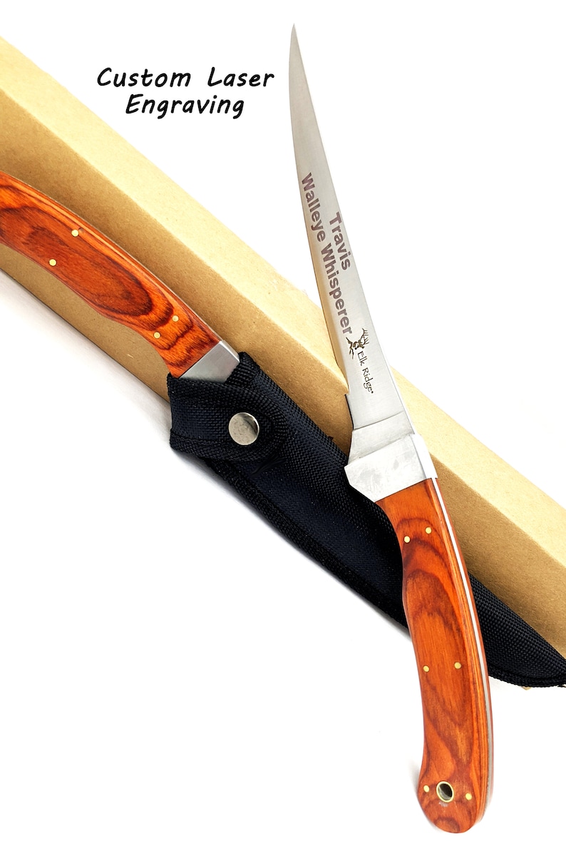 Puede incluir: Un cuchillo de caza grabado personalizado con mango de madera y funda negra. La hoja est&aacute; grabada con el texto "Travis' Walleye Whisperer Elk Ridge".