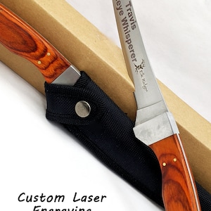 Puede incluir: Un cuchillo de pesca de acero inoxidable grabado personalizado con mango de madera marr&oacute;n. La hoja est&aacute; grabada con "Travis Walleye Whisperer Elk Ridge".