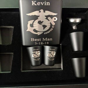 May include: A black metal flask with a silver engraving of the Marine Corps emblem and the words "Semper Fi" and "Best Man 3-18-18". The flask is in a black box with four shot glasses and a funnel.