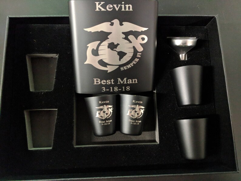 May include: A black metal flask with a silver engraving of the Marine Corps emblem and the words "Semper Fi" and "Best Man 3-18-18". The flask is in a black box with four shot glasses and a funnel.