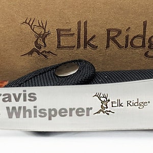 Puede incluir: Un cuchillo Elk Ridge grabado personalizado con mango de madera y hoja de acero inoxidable. La hoja est&aacute; grabada con el texto "Travis Walleye Whisperer" y el logotipo de Elk Ridge.