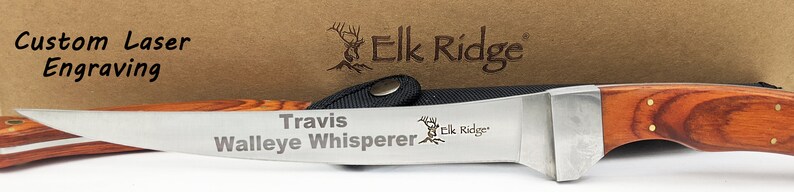 Puede incluir: Un cuchillo Elk Ridge grabado personalizado con mango de madera y hoja de acero inoxidable. La hoja est&aacute; grabada con el texto "Travis Walleye Whisperer" y el logotipo de Elk Ridge.