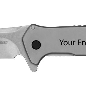 May include: A silver pocket knife with a black handle. The blade has the text "We can engrave the blade and the handle!" on it. The handle has the text "Your Engraving Here!" on it.