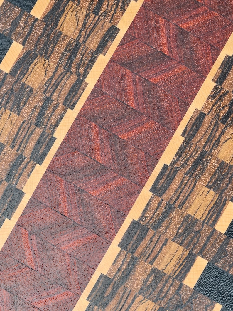 May include: A wooden chopping board with a chevron pattern in red and brown wood. The board is also made with a light wood and a dark wood with a black grain.