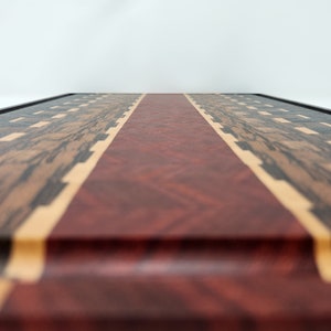 May include: A wooden chopping board with a red, white and blue design. The board is made from different types of wood, including walnut, maple and cherry.