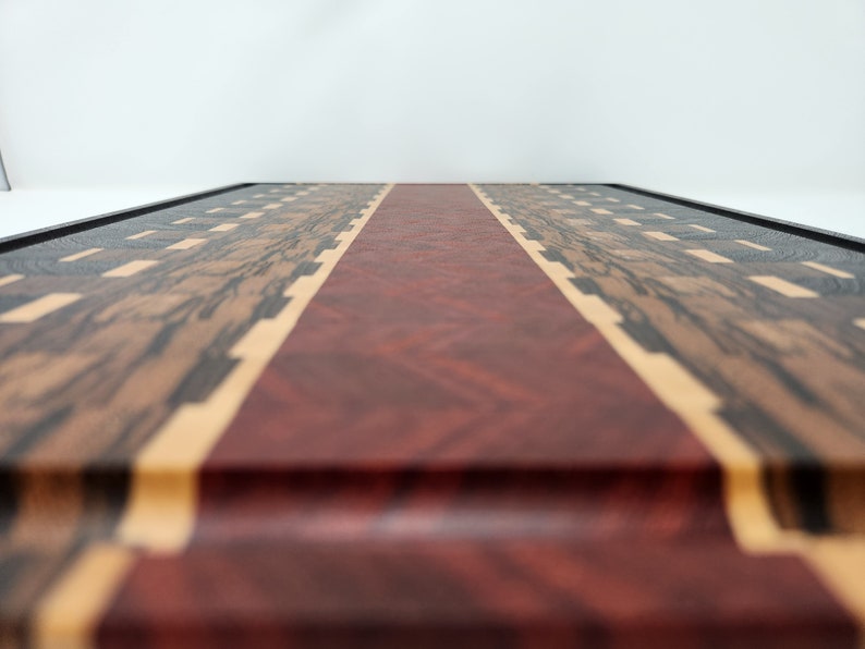 May include: A wooden chopping board with a red, white and blue design. The board is made from different types of wood, including walnut, maple and cherry.
