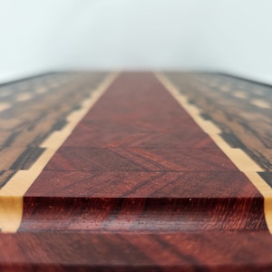 May include: A close-up of a wooden chopping board with a red centre strip and a black and brown wood border. The board has a smooth, polished finish.