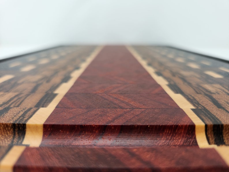 May include: A close-up of a wooden chopping board with a red centre strip and a black and brown wood border. The board has a smooth, polished finish.