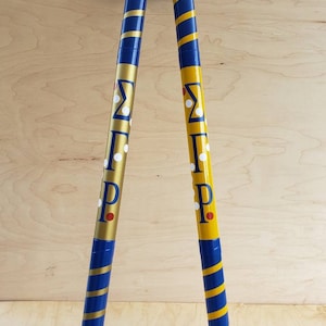Può includere: Due bastoni di legno dipinti di blu e oro con punti bianchi e rossi e le lettere "ΣΠΡ" su di essi.