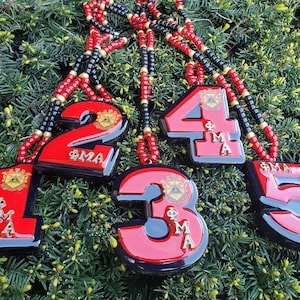 May include: Five red and black number charms with gold lettering and a black and red beaded necklace. The charms are numbered 1 through 5 and feature a Greek letter symbol and the letters "ΦΜΑ".
