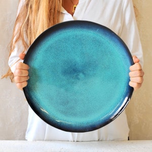 May include: A large, round, teal blue ceramic serving platter with a dark blue rim. The platter has a speckled, textured surface.