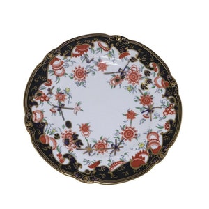 Może przedstawiać: Biały talerz porcelanowy z czarną i złotą obwódką. Talerz jest ozdobiony kwiatowym wzorem w odcieniach czerwieni, błękitu i zieleni.