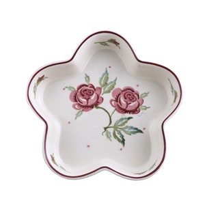 May include: A white ceramic star-shaped serving dish with a red rim and a floral design featuring two pink roses with green leaves.