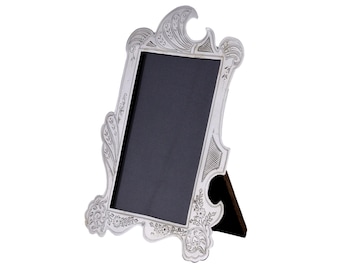 May include: A silver-plated picture frame with an ornate design. The frame has a black backing and a stand.