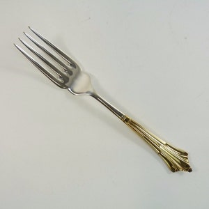 May include: A silver fork with a gold handle. The handle has a decorative design.