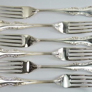 May include: Set of six silver forks with ornate handles. The forks have a polished finish and are arranged in a row.