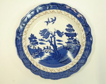 May include: A blue and white porcelain dinner plate with a traditional willow pattern. The plate has a scalloped edge and a gold trim.
