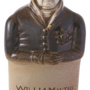 May include: A ceramic bottle with a brown glaze and a white bust of a man with a stern expression. The bottle is labeled "William Ivths Reform Cordial".
