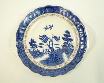 May include: A blue and white porcelain serving plate with a willow pattern design. The plate has a scalloped edge and two handles.