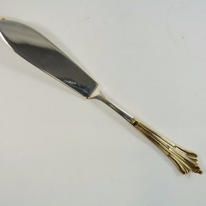 May include: A silver butter knife with a gold handle. The handle has a decorative design.