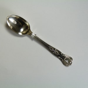 Op de afbeelding: Een zilveren theelepel met een sierlijk handvat. De lepel heeft een ronde kom en een lang, dun handvat.