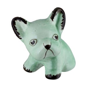 Könnte beinhalten: Hellgrüne Keramikfigur eines französischen Bulldoggen. Der Hund hat schwarze Akzente an Ohren, Pfoten und Nase. Die Augen sind herzförmig. Die Figur befindet sich in einer sitzenden Position.
