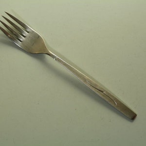 Può includere: Una forchetta d'argento con un design semplice ed elegante. La forchetta ha un manico leggermente curvo con un delicato motivo a foglia inciso.