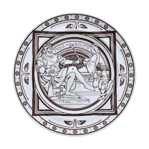 May include: White ceramic plate with a brown illustration depicting a scene from Puss in Boots. The plate has a circular design with a square central image. The illustration shows a king and a figure with a cat.