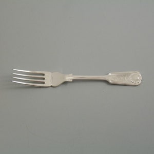 May include: A silver fork with a decorative handle. The handle features a raised design and a small circle with a design in the centre.