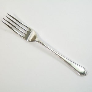 May include: A silver fork with a simple design. The fork has four tines and a rounded handle.