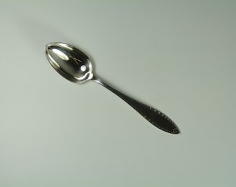 May include: A silver spoon with a rounded bowl and a decorative handle. The spoon is on a white background.