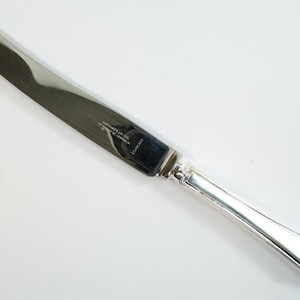 May include: A silver butter knife with a plain blade and a simple, rounded handle. The knife is marked "Carvers Ltd. Sheffield England" on the blade.