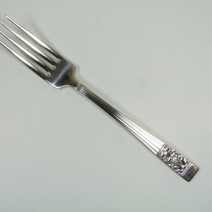 Pode incluir: Um garfo de prata com um cabo decorativo. O cabo tem um design floral.