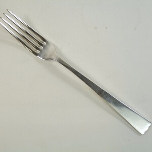 May include: A silver fork with a simple design. The fork has four tines and a slightly curved handle.