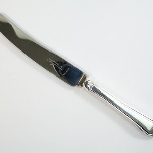 May include: A silver butter knife with a simple, elegant design. The blade is smooth and the handle has a subtle curve. The knife is marked "LAWRENCE & CO LTD SILVER PLATED" and "STAINLESS".