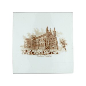 Könnte beinhalten: Quadratische, weiße Keramikfliese mit einer sepiafarbenen Illustration der Kathedrale von Winchester. Das Bild zeigt die Kathedrale, einen Friedhof und den Text "Winchester Cathedral". Die Fliese hat eine glänzende Oberfläche.