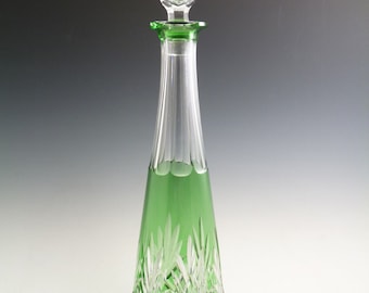 May include: A tall, clear glass decanter with a green glass base and a crystal stopper. The decanter has a cut glass design.