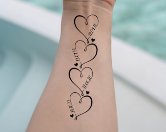 Op de afbeelding: Zwart tijdelijk tattoo-ontwerp met vier met elkaar verbonden harten met data: 24.10.22, 11.06.20, 12.09.14 en 13.01.11. Elk hart heeft een klein hartsymbool. De tattoo is op de pols aangebracht.