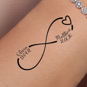 Może przedstawiać: Tatuaż w kształcie czarnego symbolu nieskończoności na nadgarstku osoby z imionami Olivia 19.04.11 i Matthew 17.06.20 oraz symbolem serca.