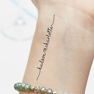 Puede incluir: Un tatuaje temporal en la muñeca de una persona con el texto "hudson & charlotte" escrito en cursiva.