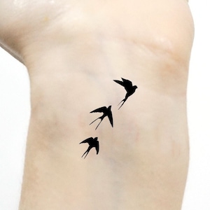 Può includere: Primo piano di un polso con un tatuaggio temporaneo di tre uccelli neri che volano in fila.